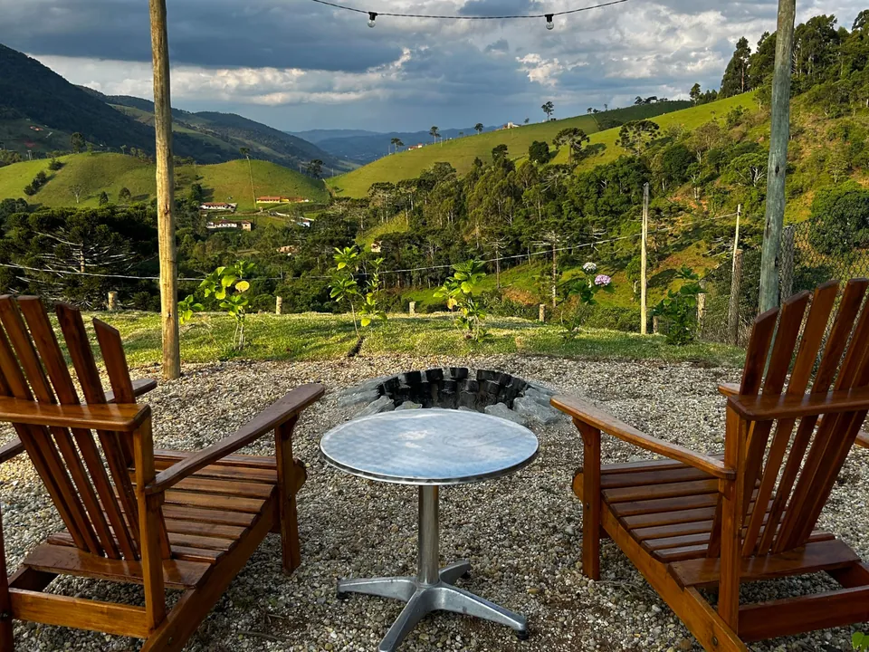 Cadeiras de madeira em volta do fogo de chão, com o vale e as montanhas ao fundo