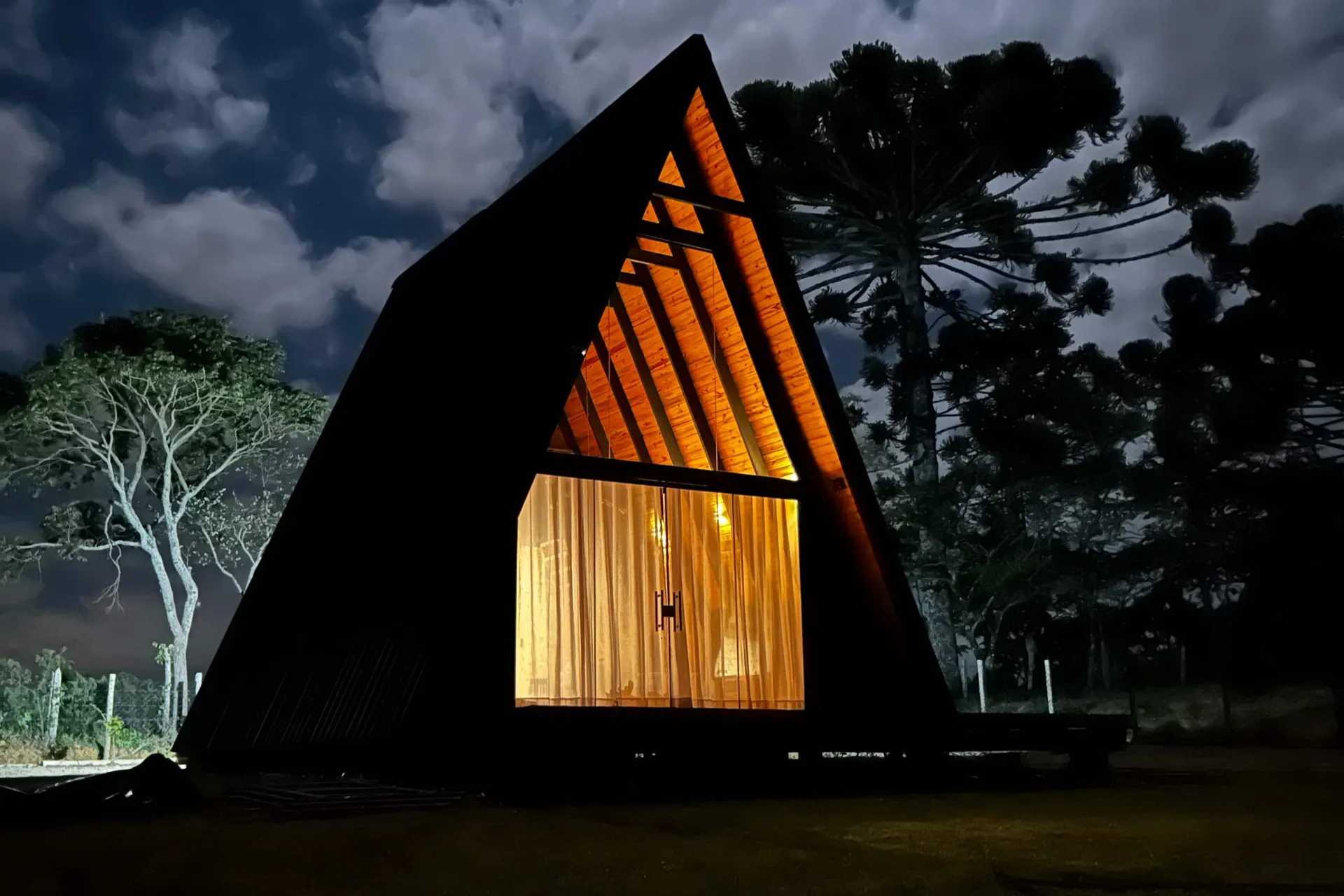 A Cabana Jequitibá iluminada à noite, com as araucárias ao fundo